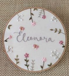 embroidered name with pink flowers and leaves on white fabric in circular wooden frame that says eleona