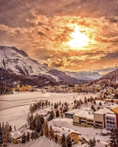 the sun is setting over a small town with mountains in the background and snow on the ground