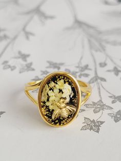 This golden plated 925 solid sterling silver features a golden bee pollinating tiny real and elderberry flowers, carefully preserved in eco resin, a statement piece of jewelry for the nature lover. This ring is made of gold plated 925 solid sterling silver Cabochon size: 14x10 mm Gift yourself or the nature lover in your life with this wearable piece of the forest that will last a lifetime. Made using eco resin, which is crystal clear, UV stable (which means it won't turn yellow over time), does Gold Oval Flower Ring With Birth Flower Detail, Gold Rings With Pressed Flowers For Wedding, Nature-inspired Gold Flower Ring With Birth Flower, Nature-inspired Gold Birth Flower Ring, Gold Ring With Pressed Flowers, Elderberry Flower, Eco Resin, Golden Ring, Ethical Jewelry