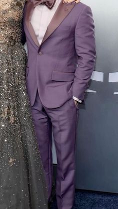 a man in a purple suit and bow tie standing next to a woman in a gray dress