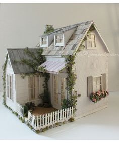 a doll house with a white picket fence and flowers in the window boxes on top