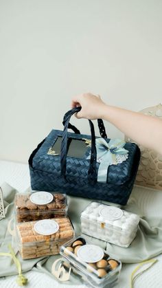 a person holding a blue bag next to some food on a bed with white sheets