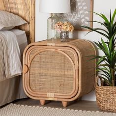 a wicker side table next to a bed with a plant on it and a lamp