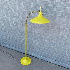 a yellow floor lamp next to a brick wall