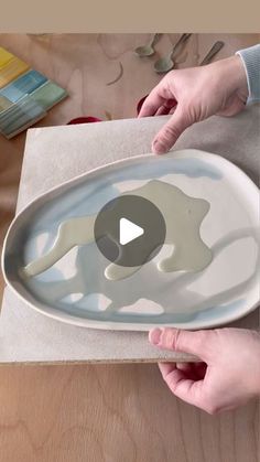 two hands are holding a white plate with some liquid on it