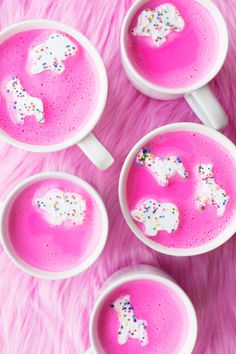 four mugs filled with pink liquid and sprinkles on top of a pink blanket