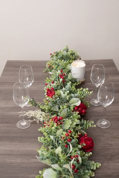 the table is set with red roses and greenery on it, along with wine glasses