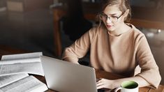 a woman sitting at a table with a laptop computer and papers in front of her