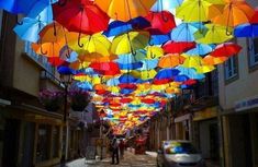 many colorful umbrellas are hanging from the ceiling in an alleyway with people walking under them