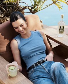 a woman sitting on top of a wooden bench next to a bottle