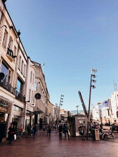 people are walking down the street in front of some buildings and shops on a sunny day