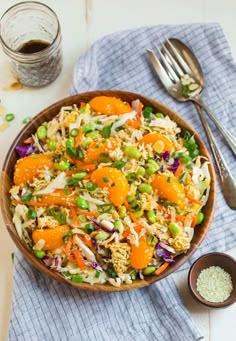 a bowl filled with rice, carrots and peas next to two spoons on a table