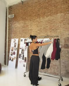 a woman standing in front of a brick wall with clothes hanging on racks next to her