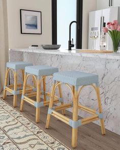 three stools in front of a counter with flowers on it and an area rug