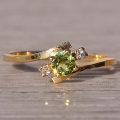 two gold rings with green and white stones on wooden table next to each other,