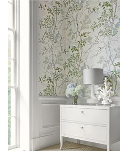 a white dresser sitting in front of a window next to a wallpapered wall