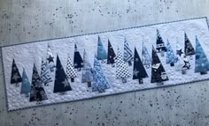 a quilted wall hanging with blue and white christmas trees on it's side