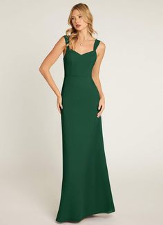 a woman in a long green dress with straps on the back and shoulders, standing against a