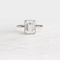 an emerald - cut diamond ring sits on a white surface