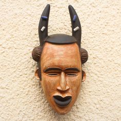 Inspired by the masks used by the Igbo people of Nigeria Ghana's Christopher Nyasafo designs a striking African mask that depicts a traditional water spirit. This hand-carved sese wood mask which features a brown rustic face has squinted eyes and black lips. The spirit's black horns are accented with four beads of recycled glass. Squinting Eyes, Black Horns, Traditional Masks, Wood Mask, Water Spirit, African Mask, Recycled Glass Bead, Black Lips, African Masks