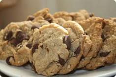 chocolate chip cookies stacked on top of each other on a white plate with a glass of milk in the background