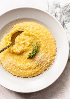 mashed potatoes in a white bowl with a spoon on the side and sprigs of rosemary