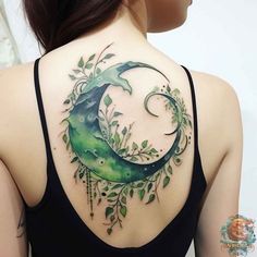 the back of a woman's shoulder is covered with green leaves and an crescent tattoo