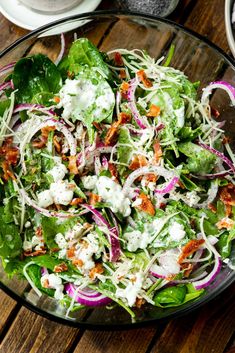 a salad with lettuce, carrots and feta cheese in a glass bowl