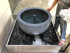 a man standing next to a sink in a room filled with black rocks and water