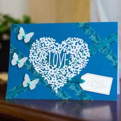 a blue card with white flowers and butterflies in the shape of a heart that says i love you