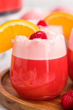 two glasses filled with liquid and fruit on a wooden tray next to oranges, raspberries, and lemon wedges