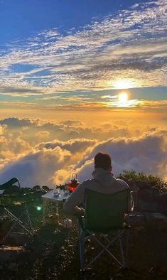 a man sitting in a chair on top of a mountain with the sun behind him