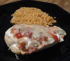 a black plate topped with meat covered in cheese and sauce next to rice on a wooden table