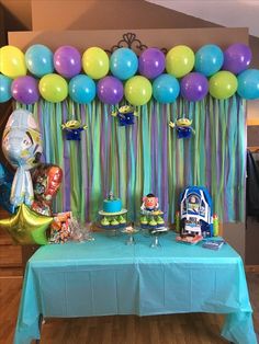 a table topped with balloons and cake next to a blue table cloth covered tablecloth