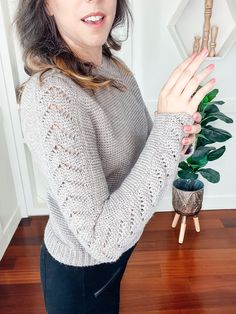 a woman standing in front of a houseplant holding her hand up to the camera