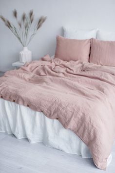 an unmade bed with pink linens in a white room next to a potted plant