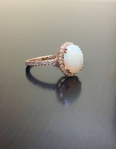 DeKara Designs Collection Our latest design! An elegant and lustrous Opal cabochon surrounded by beautiful diamonds in a halo setting. Metal- 18K Rose Gold, .750. This Specific Ring Is a Size 6 3/4 Stones- Center Features an Oval Fiery Australian Opal Cabochon Cut 2.20 Carats, 11.10 MM Long, 9 MM Wide, 44 Round Diamonds, H-I Color VS2-SI1 Clarity, 0.40 Carats. Latest of my creations. A beautiful Opal Halo Diamond Ring. The Opal is professionally prong set in between 4 double prongs. There are 10 Elegant Diamond Opal Ring With Brilliant Cut, Elegant Opal Ring With Brilliant Cut Diamond, Elegant Diamond White Opal Ring, Elegant White Gold Opal Ring With Brilliant Cut, Elegant Diamond White Opal Ring With Prong Setting, Elegant Opal Ring With Diamond Accents In White Gold, Elegant White Gold Opal Ring With Diamond Accents, Rose Gold Round Cut Gemstone Halo Ring, Exquisite Rose Gold Halo Setting Ring