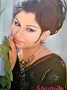 the woman is posing with her hand on her face and holding a plant in front of her