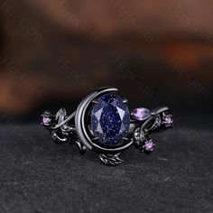 a ring with an oval shaped blue stone surrounded by leaves and pink stones on top