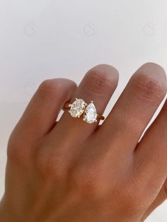 a woman's hand wearing a gold ring with two pear shaped diamonds