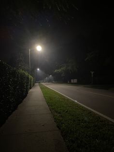 an empty street at night with the lights on and grass growing along the curb area