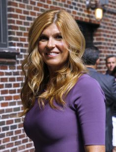 a woman with long blonde hair is standing in front of a brick building and smiling