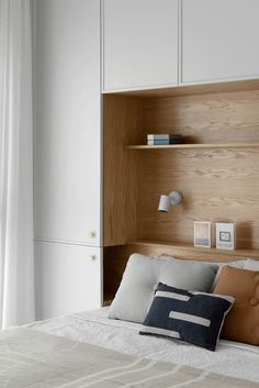 a bed with white and wood headboard next to a wall mounted book shelf in a bedroom