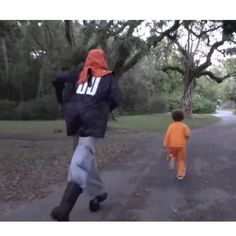 two people walking down a road with trees in the background and one person wearing an orange hoodie