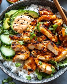 a bowl filled with chicken, cucumber and rice next to chopsticks