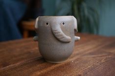 an elephant cup sitting on top of a wooden table next to a potted plant