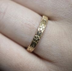 a gold wedding band with flowers and leaves on the inside, in someone's hand