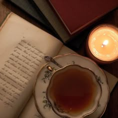 an open book next to a lit candle and teacup on a plate with saucer