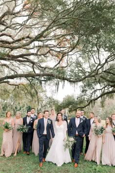 a bride and groom with their bridal party in front of the trees at this wedding