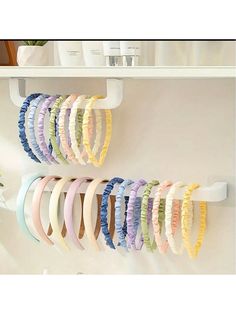 several different colored hair ties hanging on a white wall next to a vase with flowers